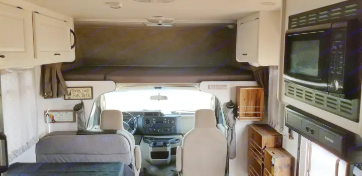 Spacious rv rental interior with cockpit, overhead bunk, and kitchen appliances including microwave. Cozy decor signs visible.. Thor Majestic 2013
