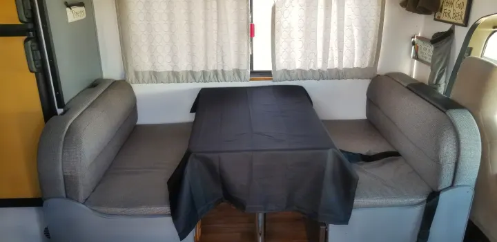This RV rental dinette has gray benches, a black table, and window curtains, with a refrigerator on the left.. Thor Majestic 2013