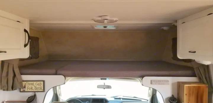 View from inside an RV rental looking towards the front. Overhead bunk, driver's cabin, white cabinets, & humorous signs.. Thor Majestic 2013