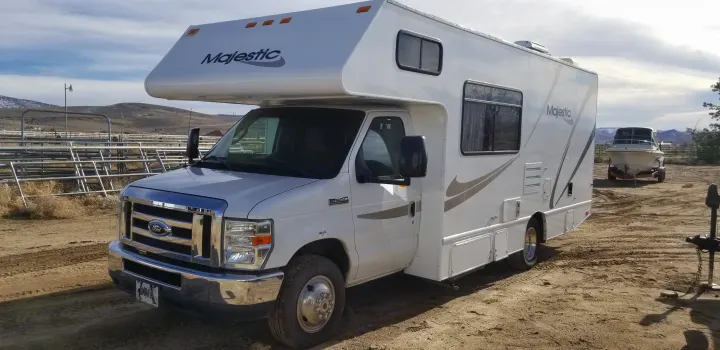 This white Majestic RV rental (Ford E-350 Class C) is parked on dirt, ready for adventure, with mountains and a boat behind.. Thor Majestic 2013