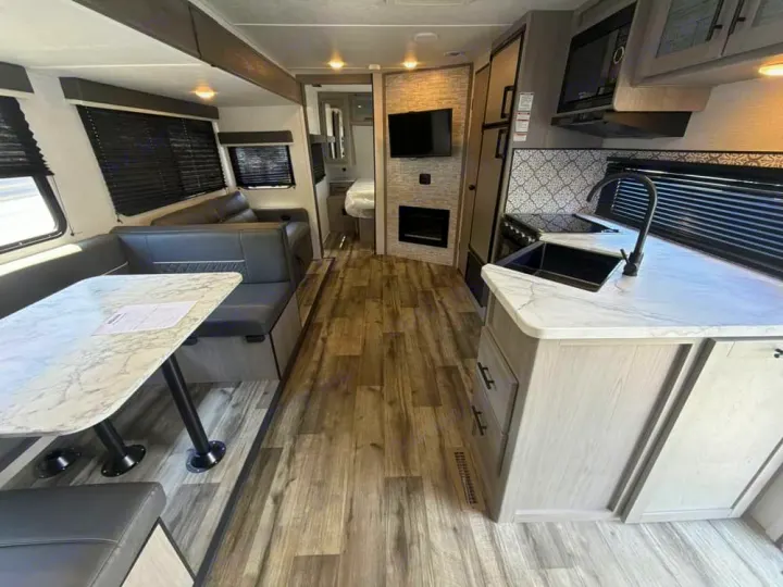 Spacious RV rental interior featuring a modern kitchen, dining area, lounge with fireplace, and peek into the bedroom.. Dutchmen Coleman Light 2022