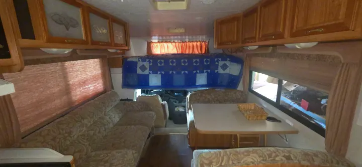 Spacious rv rental interior with patterned couch, dining area, kitchen, and overhead bed. Perfect for your next adventure!. Coachmen Leprechaun 2009