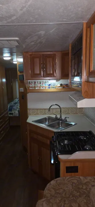 A cozy RV rental interior: kitchen with wood cabinets, sink, stove, microwave, and a glimpse of the bedroom. Perfect for trips.. Coachmen Leprechaun 2009