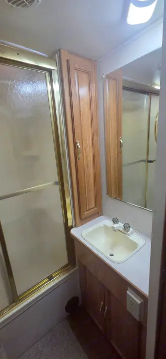 This compact RV rental bathroom features a shower with frosted glass, a sink with mirror, and warm wood cabinetry.. Coachmen Leprechaun 2009