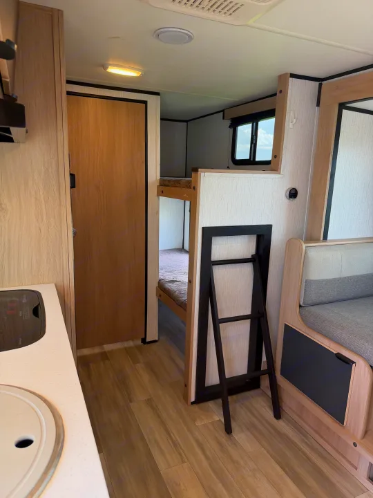 Inside this modern rv rental: a light-toned kitchen counter, a closed door, cozy bunk beds with a ladder, and dinette seating.. Cruiser RV Hitch 2022
