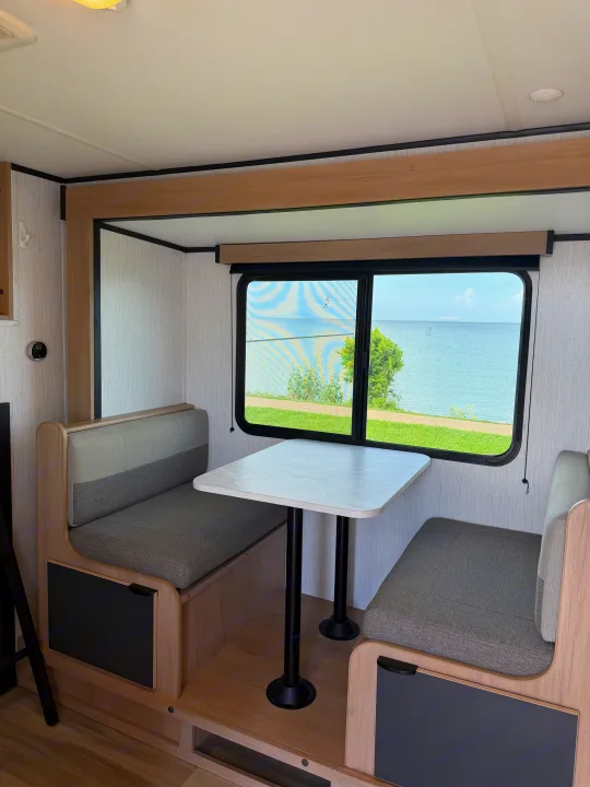 Cozy RV rental dinette with waterfront view. Light wood and grey seating create a modern, comfortable space inside.. Cruiser RV Hitch 2022