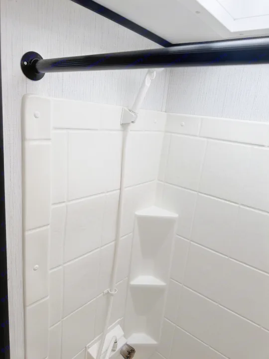 Inside an RV rental shower: white tiled walls, handheld shower, and corner shelf. Functional for your road trip.. Cruiser RV Hitch 2022