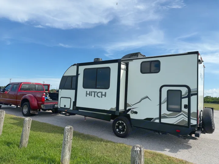 Red truck towing a white Hitch RV rental with an extended slide-out under a blue sky, ready for a camping trip.. Cruiser RV Hitch 2022