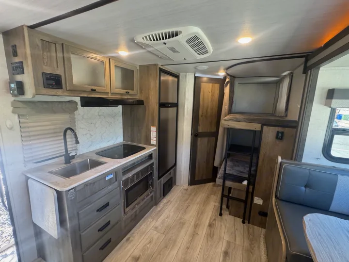 Modern RV rental interior: full kitchen with microwave & sink, refrigerator, dinette, and cozy bunk beds.. Forest River Surveyor Legend 2023
