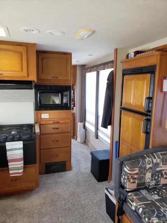 RV rental's compact interior: kitchen with wood cabinets, microwave, stove, paneled fridge, patterned sofa, and carpet.. Fleetwood Tioga 31M 2007