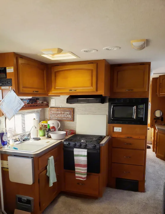 Compact RV rental kitchen features a sink, stove, microwave, and wood cabinets, ready for camp cooking.. Fleetwood Tioga 31M 2007