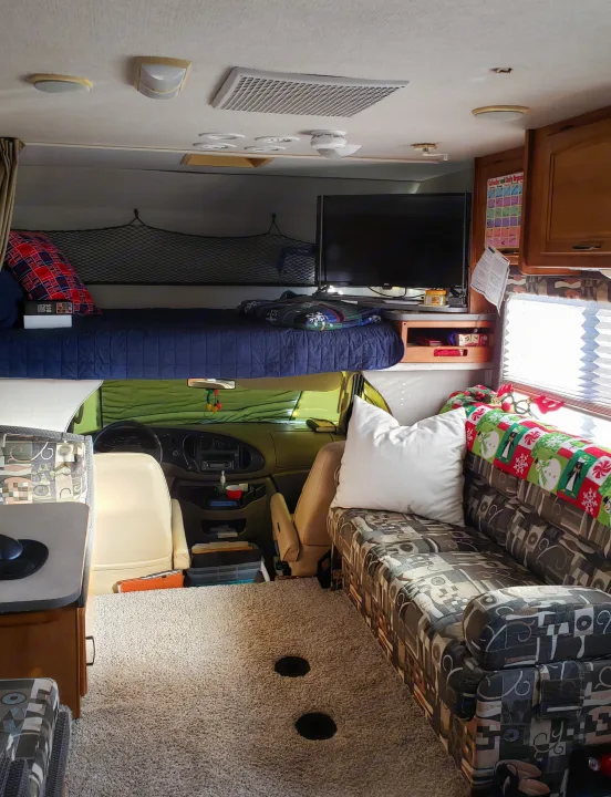 Cozy RV rental interior: overhead bunk, patterned sofa, TV, & unique floor holes (possibly for ice fishing). Ready for adventure!. Fleetwood Tioga 31M 2007