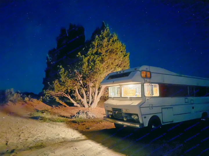 Starry night over a white RV rental parked by a large tree. Warm interior lights glow, a cozy retreat in nature.. International 510A 1973