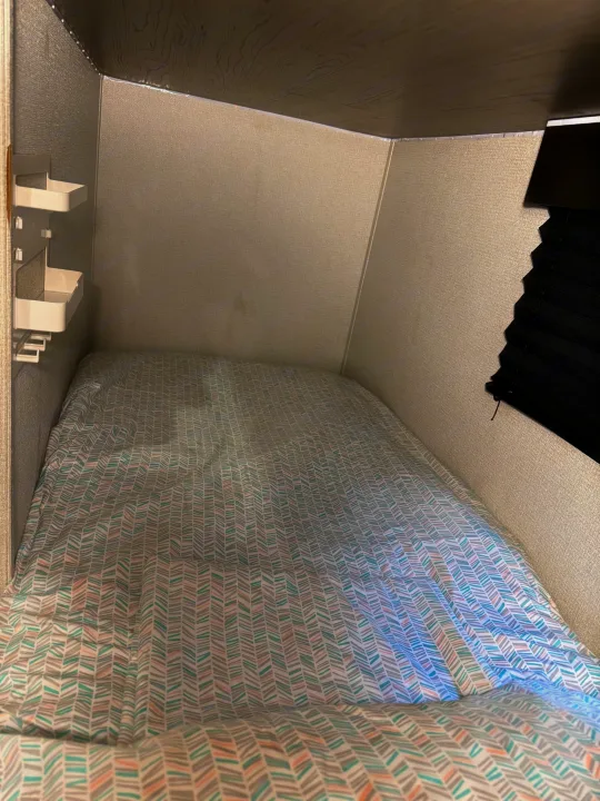Cozy sleeping bunk in an RV rental featuring patterned bedding, textured walls, a wooden ceiling, and small shelves.. Keystone RV Hideout 2021