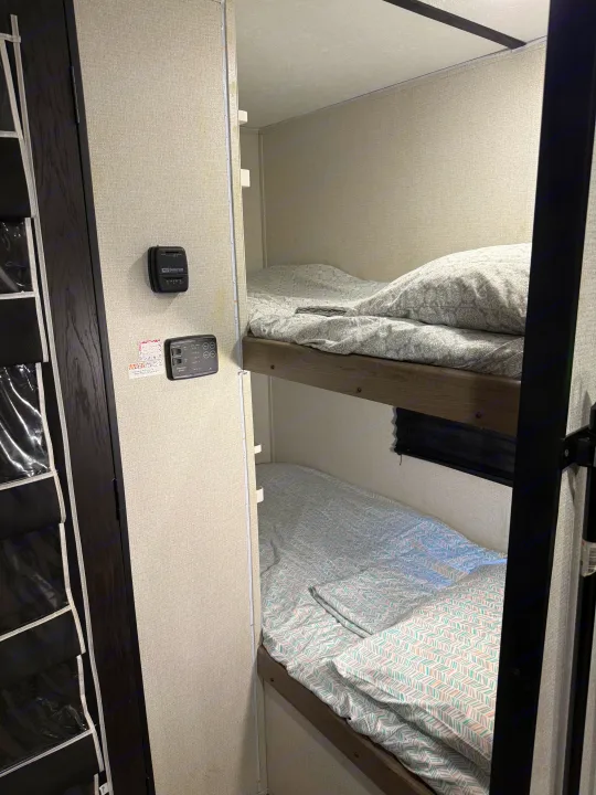 RV rental interior: Two cozy bunk beds with patterned bedding, a wall-mounted thermostat, and system controls.. Keystone RV Hideout 2021