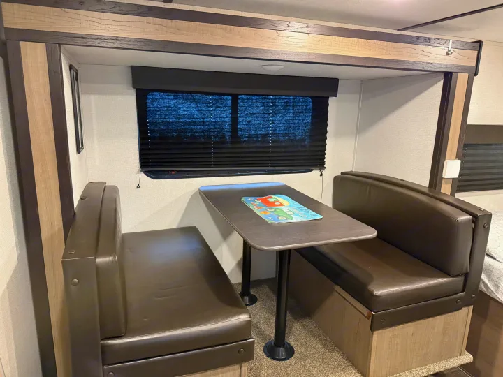 RV rental dinette: A cozy dining area with dark benches, a table, and a window with dark blinds.. Keystone RV Hideout 2021