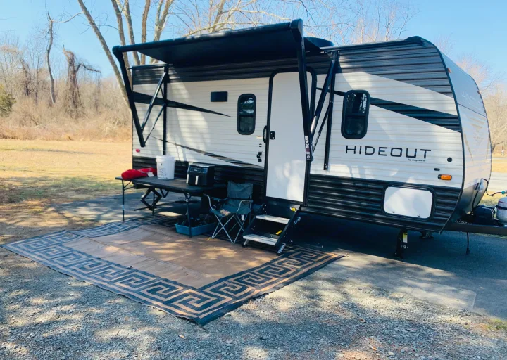 RV rental travel trailer setup with extended awning, outdoor mat, table, and chair for camping.. Keystone RV Hideout 2021