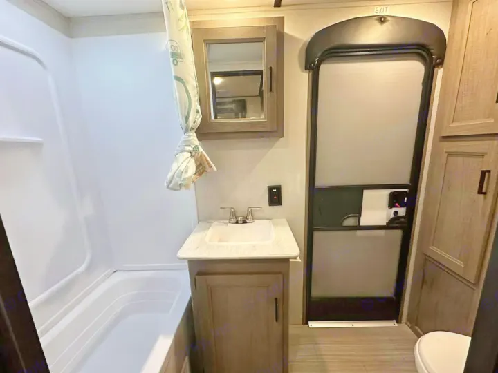 Experience comfort in this RV rental bathroom, featuring a shower/tub, vanity, mirror, toilet, and exit door.. Keystone RV Hideout 2021
