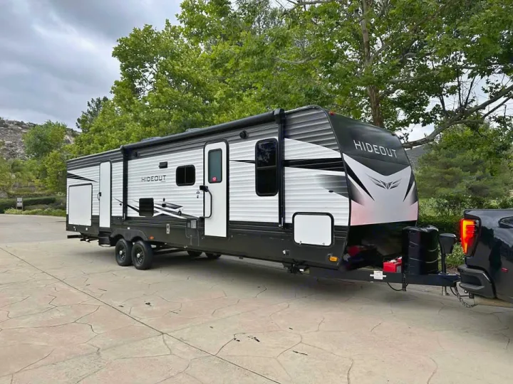 This large white and black Hideout travel trailer, an excellent RV rental option, is hitched to a truck on a paved drive.. Keystone RV Hideout 2021