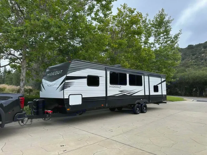 Modern HIDEUT rv rental travel trailer, black & white, hitched to a dark pickup truck, parked outdoors. Ready for adventure!. Keystone RV Hideout 2021