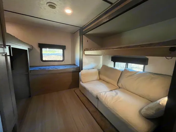 Explore this RV rental's spacious bunkhouse, featuring a cozy white sofa, bunk beds, and natural light from windows.. Keystone RV Hideout 2021