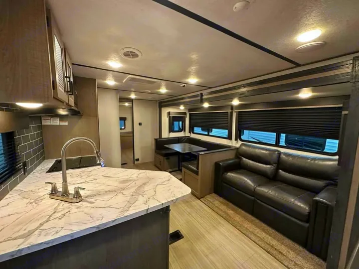 Spacious RV rental showcasing a modern kitchen with marble-look counters, comfortable dinette, and black leather sofa.. Keystone RV Hideout 2021