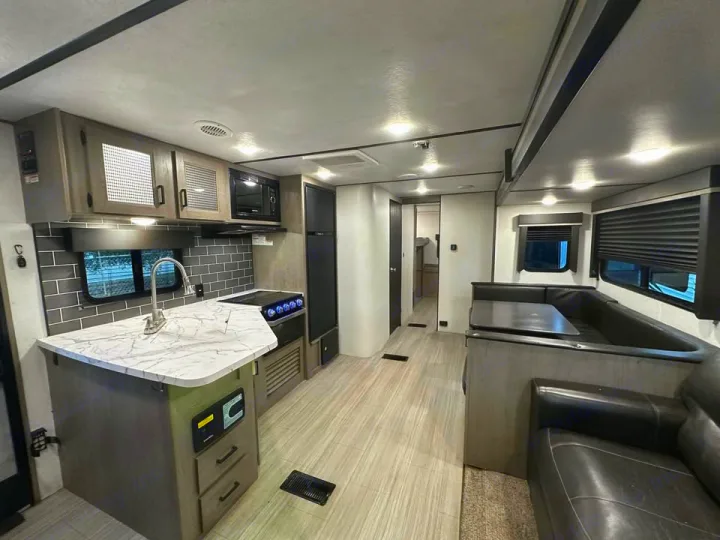 Modern RV rental interior: spacious kitchen with dark subway tile, dining booth, and cozy seating. Perfect for adventure!. Keystone RV Hideout 2021