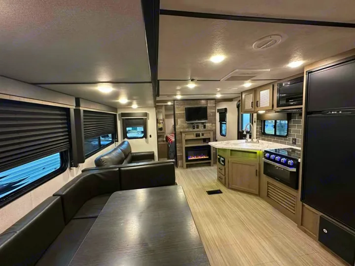 This RV rental's modern interior features a kitchen island, dark sofa, dining area, TV, and electric fireplace.. Keystone RV Hideout 2021