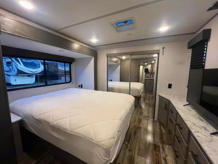 RV rental's spacious, modern bedroom featuring a large bed, mirrored closet, TV, and storage for a comfortable journey.. Keystone RV 3055bs 2022