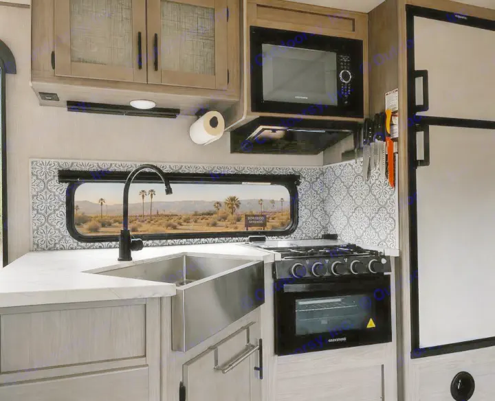 RV rental kitchen showcasing a modern sink, stove, microwave, and a scenic desert window view. Great for your next road trip!. Keystone RV 3055bs 2022