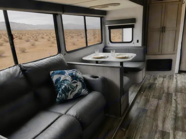 Inside a spacious RV rental: a grey sofa, dining area, and large windows revealing a vast desert landscape.. Keystone RV 3055bs 2022