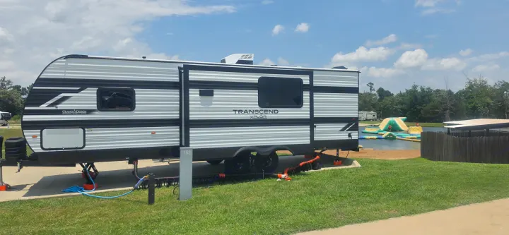 RV rental: Grand Design travel trailer parked at a sunny lakefront campsite with an inflatable water park in the background.. Grand Design Transcend Xplor 26BHX 2027