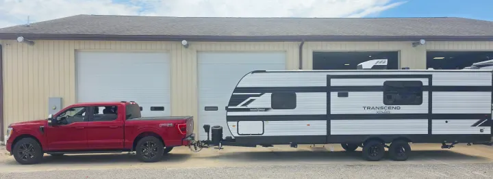 Red pickup truck towing a Grand Design Transcend Xplor travel trailer (an RV rental) outside a garage building.. Grand Design Transcend Xplor 26BHX 2027