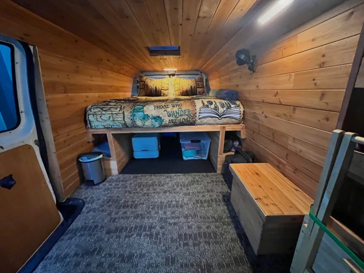 RV rental: Cozy wood-paneled camper van interior features a bed, under-bed storage, and carpeted floor.. Ford Econolline 250s 1998