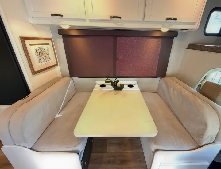 Cozy RV rental dinette interior featuring light-colored booth seating, a table, and white overhead cabinets for your travels.. Thor Four Winds 2019