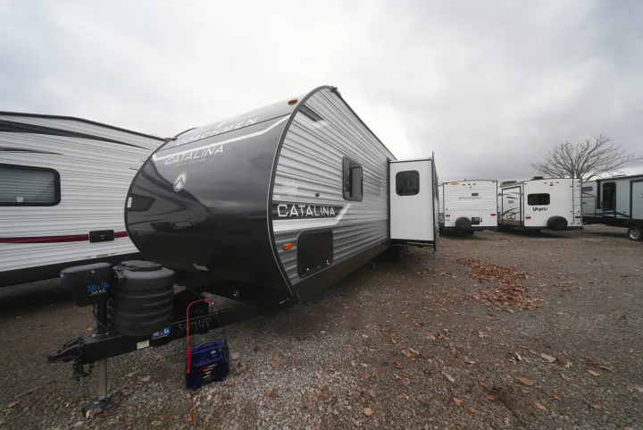 A "Catalina Legacy Edition" travel trailer and other RVs parked on a gravel lot under a cloudy sky, suitable for RV rental.. Catalina 293TQBSCK 2025