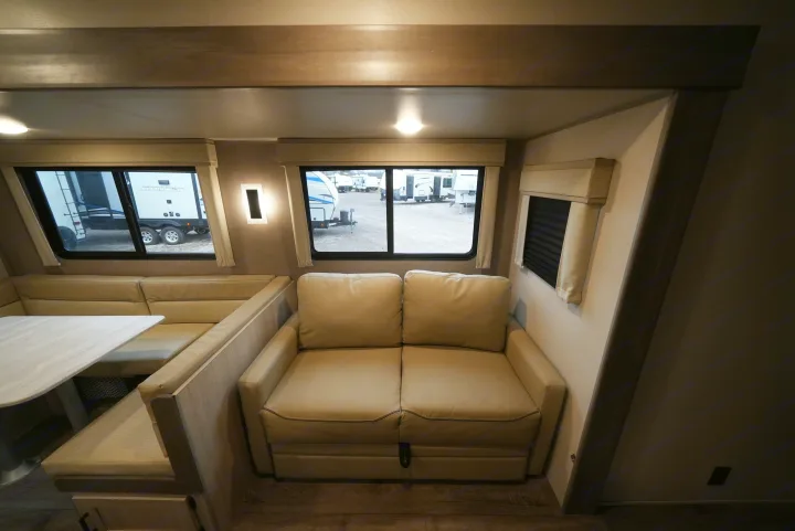 Spacious RV rental interior with a dinette, pull-out sofa, and bright windows showing other RVs outside.. Catalina 293TQBSCK 2025
