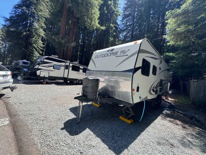 RV rental adventure amidst towering trees! White travel trailers parked on a gravel campsite, with a Jeep in view.. Outdoors RV Blackrock 2017