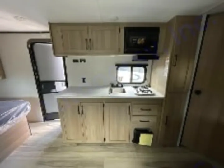 Modern RV rental kitchen with light wood cabinets, sink, 2-burner stove, microwave, & fridge. Ready for travel cooking!. Keystone Coleman 19B 2026