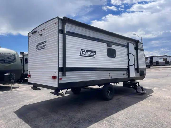 This silver and black Coleman travel trailer, ideal for an RV rental, is parked on asphalt under a cloudy sky.. Keystone Coleman 19B 2026