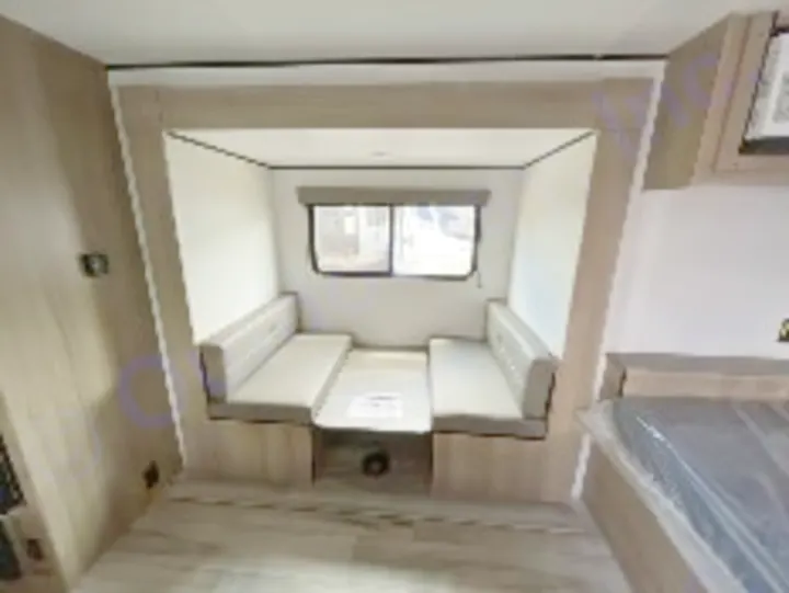 This RV rental features a cozy dinette with two cushioned benches, a table, and a large window, framed by light-toned walls.. Keystone Coleman 19B 2026