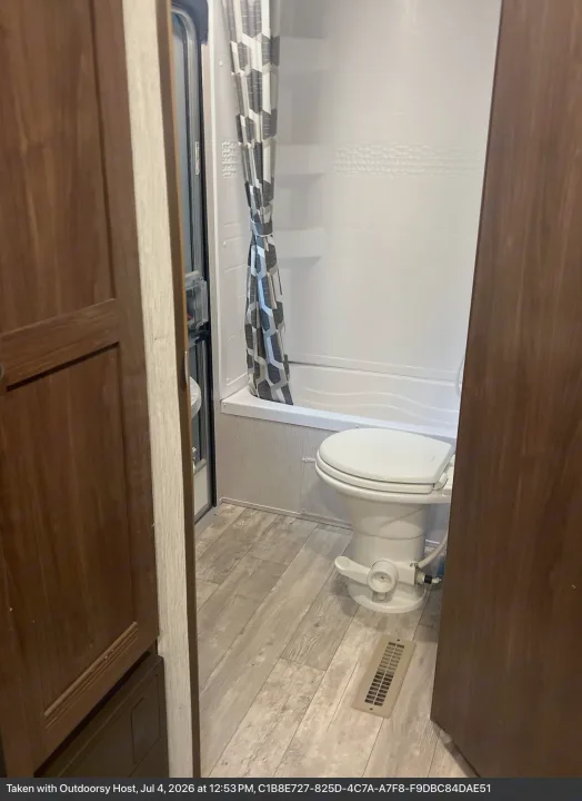 Compact RV rental bathroom featuring a white toilet, a small tub/shower combo, and a patterned shower curtain.. Heartland RVs Pioneer 2018