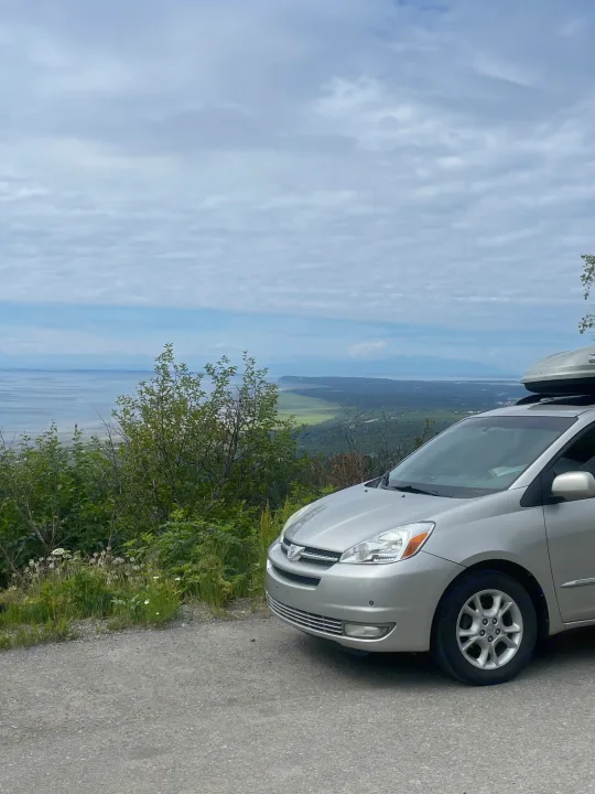 Silver minivan with roof box at a scenic overlook, vast bay, green land & mountains, like an RV rental adventure.. Toyota Sienna Limited XLE Camper Van 2004
