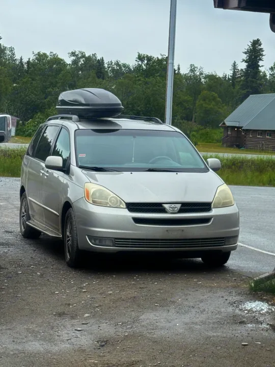 Silver minivan with a roof box, parked on gravel. Perfect for road trips, like exploring with an RV rental.. Toyota Toyota Sienna XLE 2005