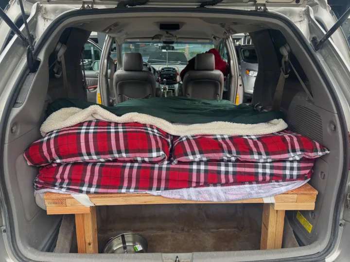 Inside a minivan, a DIY wooden bed platform with plaid bedding offers a cozy sleep setup, great for an RV rental alternative.. Toyota Toyota Sienna XLE 2005