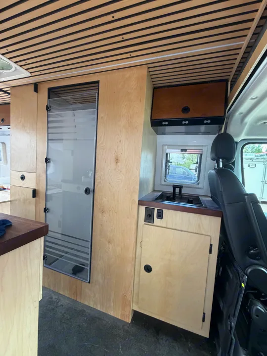 RV rental van conversion: modern interior with wood slat ceiling, light cabinetry, kitchenette, and frosted glass shower.. Safari Safari 2025