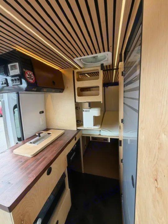 Modern RV rental interior showcasing a compact kitchenette, cozy bed, and slatted wood ceiling with integrated lighting.. Safari Safari 2025