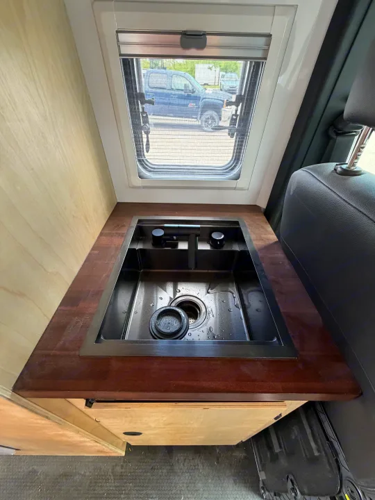 RV rental: Camper van kitchenette with dark sink, wood counter, and window. A vehicle seat is visible on the right.. Safari Safari 2025