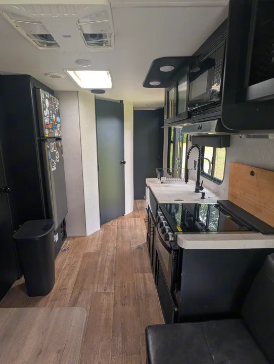 Bright travel trailer rv rental kitchen with black appliances, white counters, wood floor, and seating area.. Forest River Cherokee Grey Wolf 2021