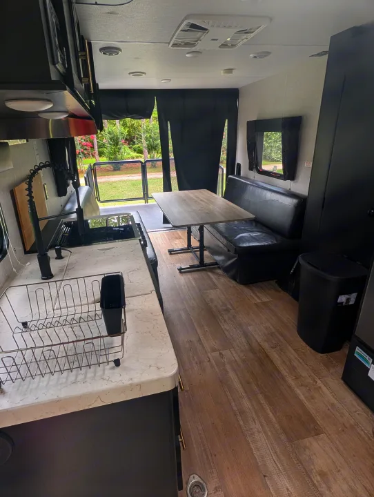 Spacious RV rental interior: modern kitchen with sink, dining area with black bench seating, and outdoor views from the open rear.. Forest River Cherokee Grey Wolf 2021
